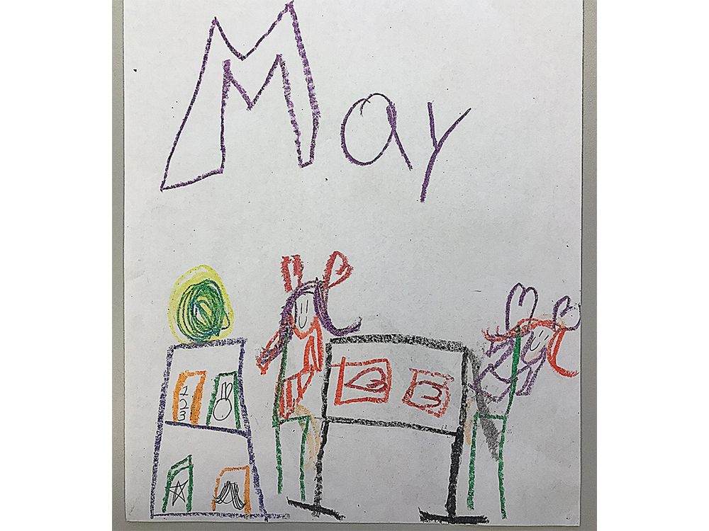 Drawing by a second grader that shows two girls standing next to a building that is probably Hope. A table is between them and big letters that say May on top of the page.